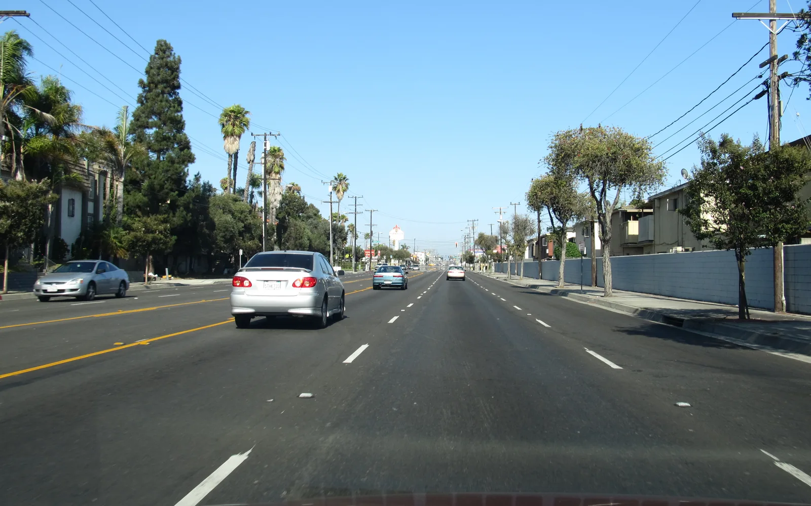 Tree-lined street in a residential area with parked cars and storefronts